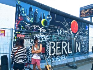 Man Wearing Black Waistcoat and White Tank Tops Standing Near a Mural in Berlin